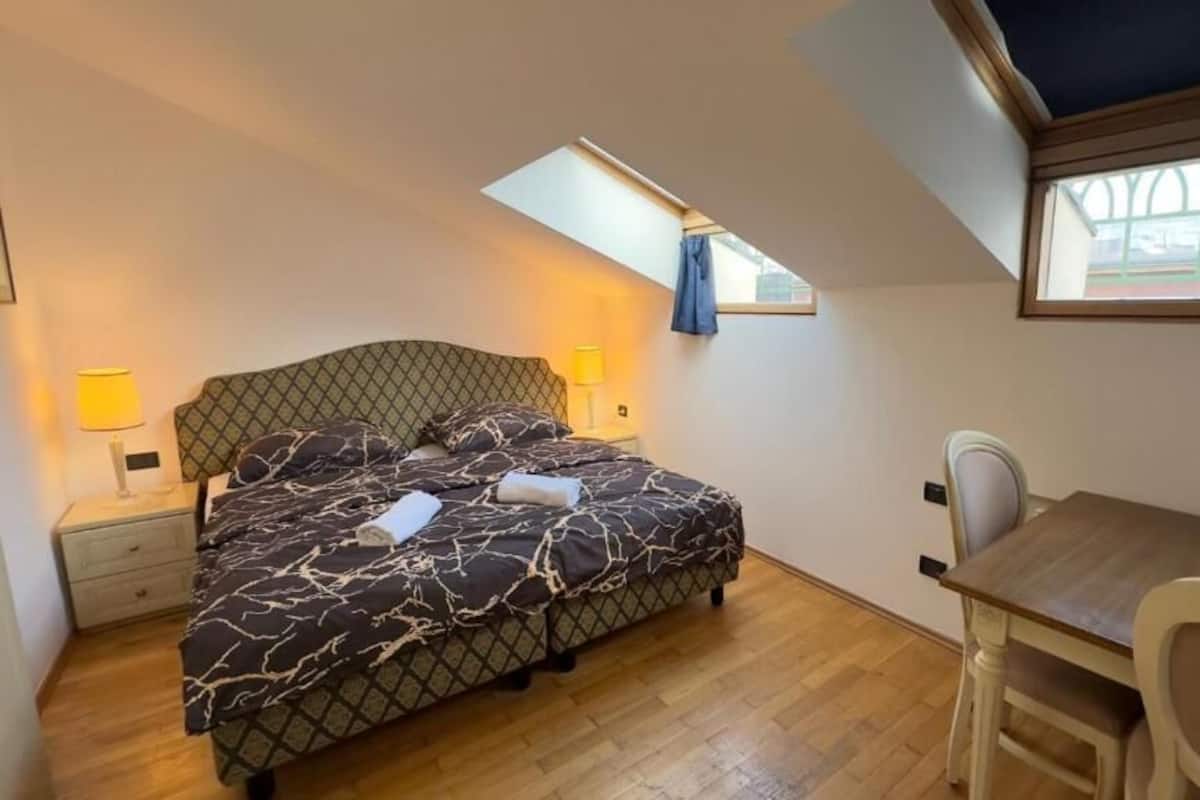 A bedroom with a bed, bedside tables, a desk, and a chair.