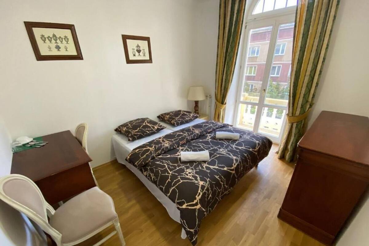 A bedroom with a bed, a desk, a chair, and a window with curtains.