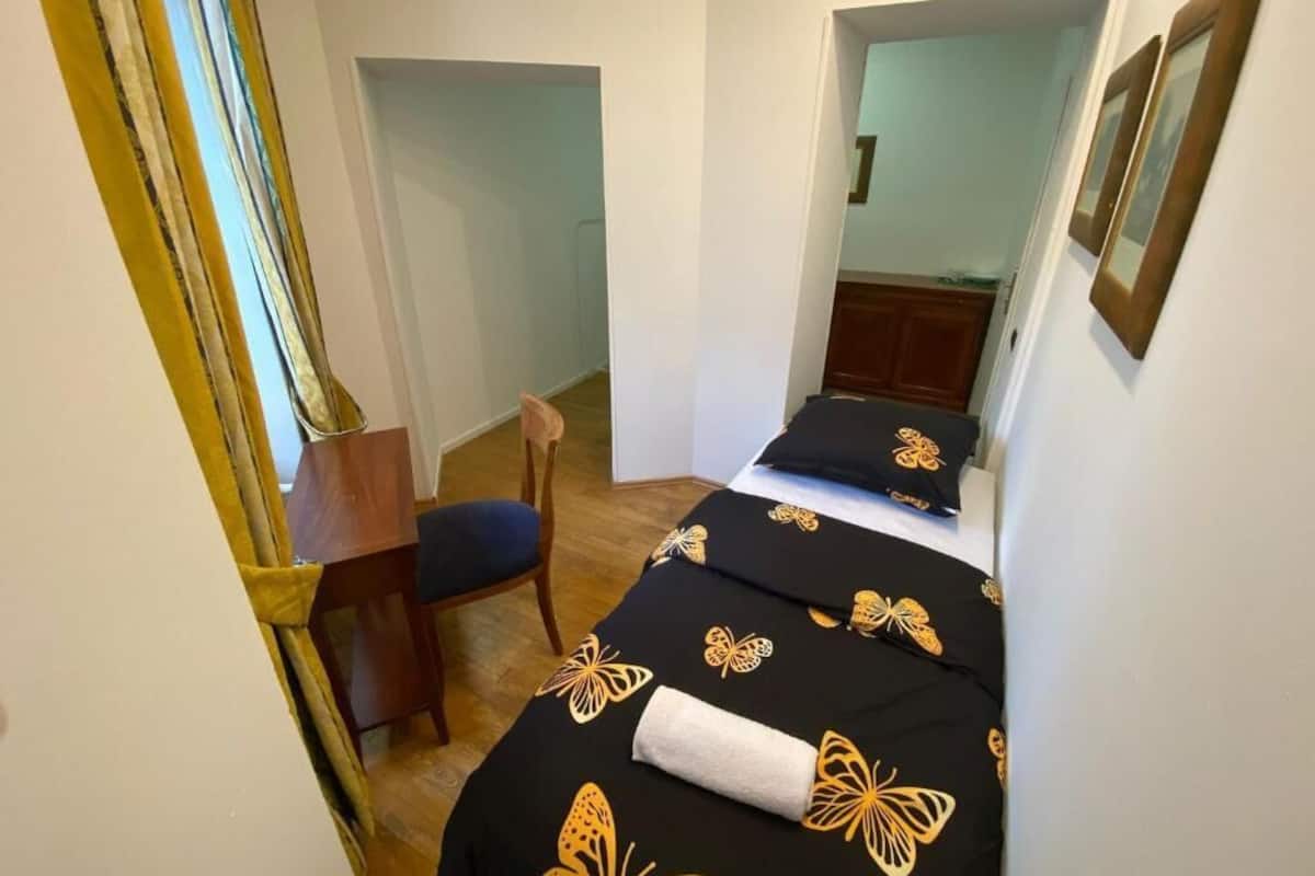 A narrow room with a bed, a chair, and a small table.