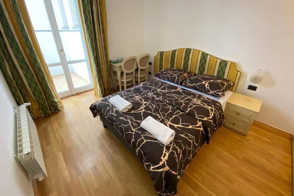 A bedroom with a bed, a nightstand, a chair, and a window with curtains.