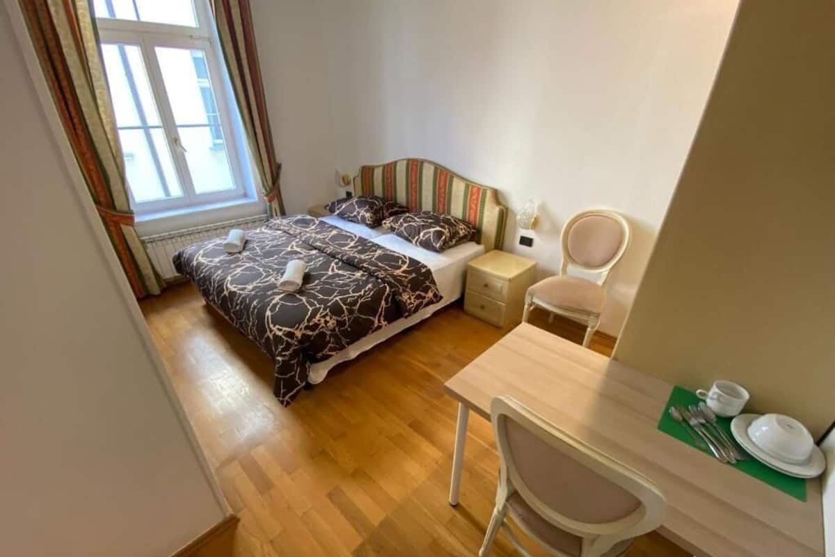 A bedroom with a bed, bedside table, chair, and a small desk area with a cup and saucer.