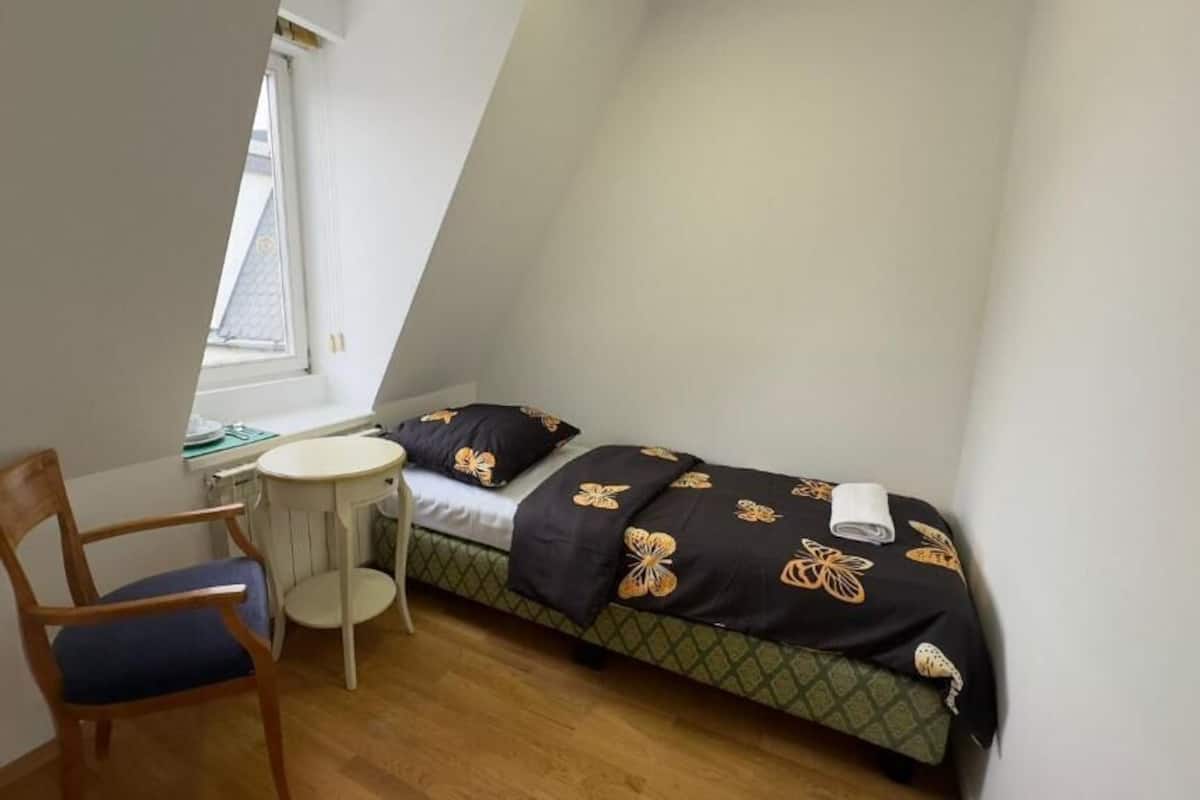 A small, triangular room with a bed, a chair, and a small table.