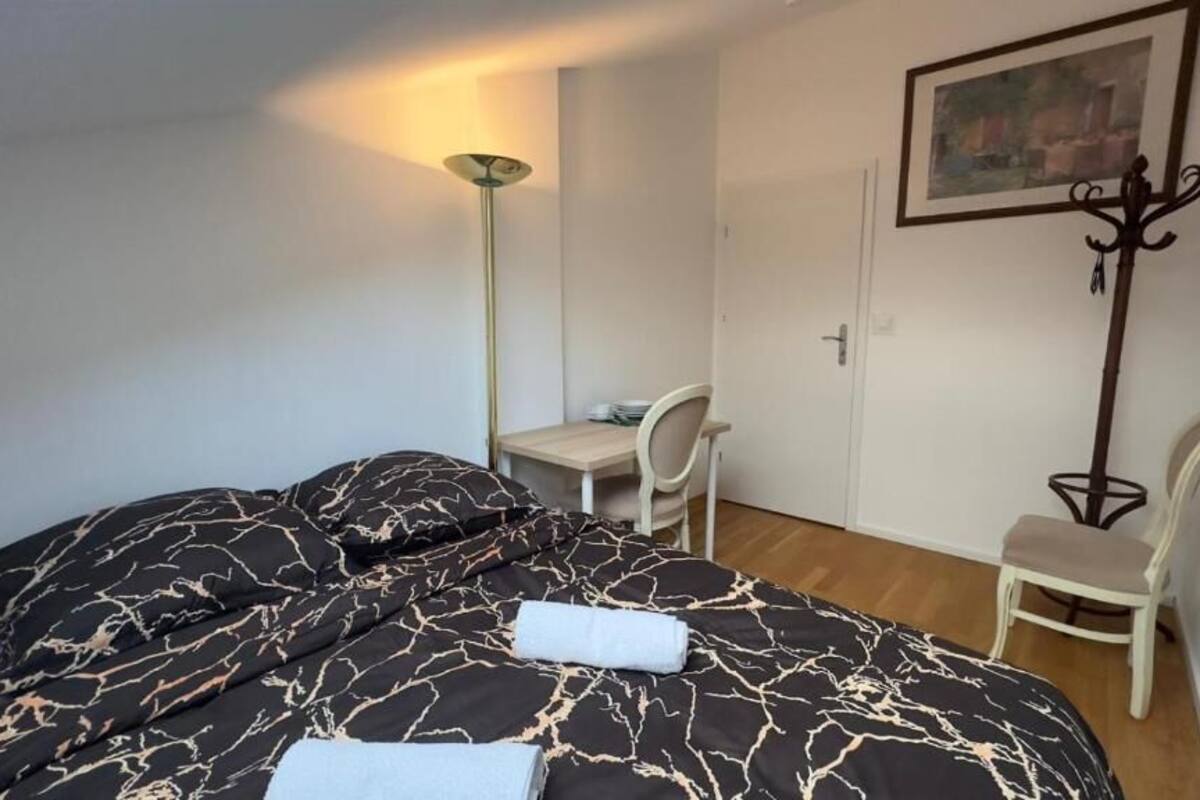 A bedroom with a bed, a desk, a chair, and a coat rack.