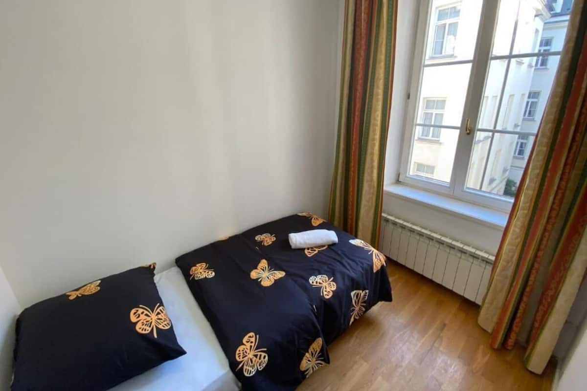A small, single-bed room with a window, striped curtains, and a radiator.