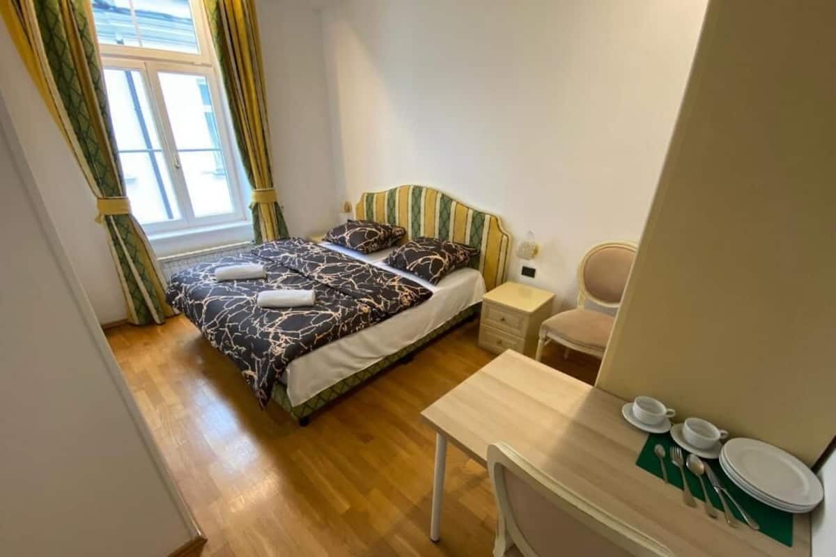 A bedroom with a bed, a desk, a chair, and a window with curtains.