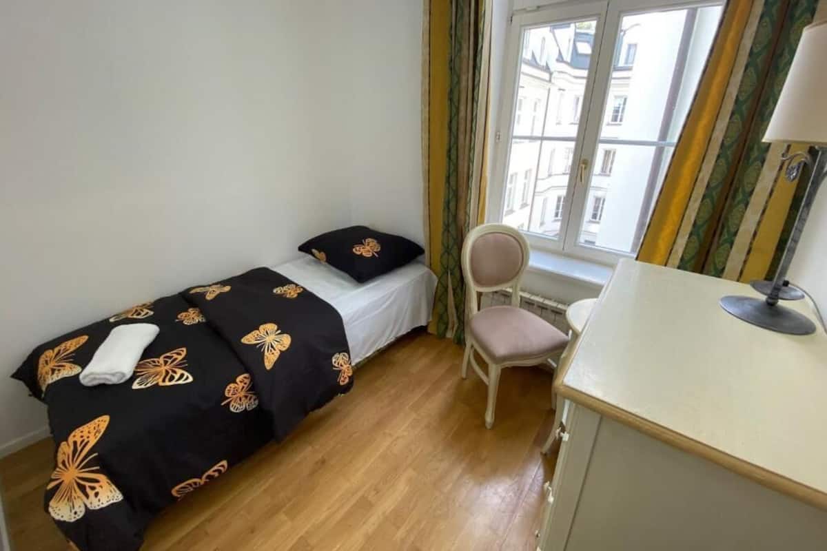 A small room with a bed, a chair, a desk, and a window with curtains.