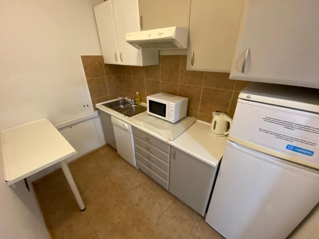 A compact kitchen with white cabinets, a microwave, a coffee maker, and a refrigerator.