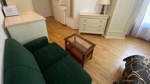 Una sala de estar con un sofá verde, una mesa de centro de madera, un armario blanco y una lámpara.