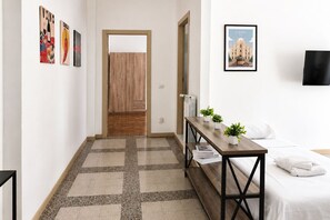 Une chambre d’hôtel avec un lit, une table de chevet ornée d’une plante, un tableau encadré au mur et une porte donnant sur une autre pièce.