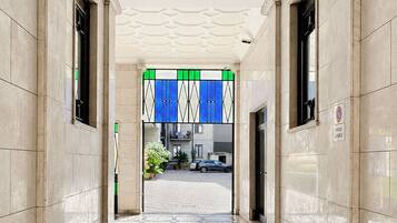 A corridor with a patterned floor, a ceiling with a geometric design, and a view into a building with a blue and white striped awning.
