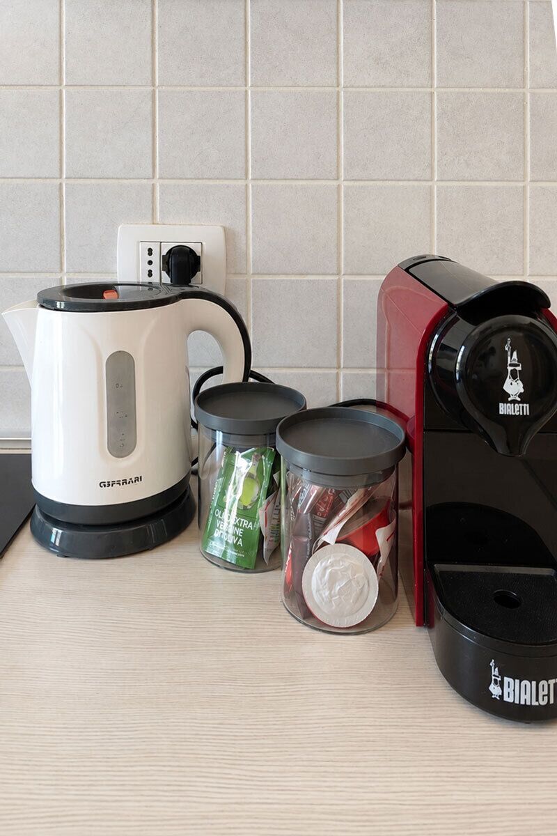 Un piano di lavoro da cucina con un bollitore elettrico bianco, una macchina del caffè rossa e due contenitori di vetro con coperchi.