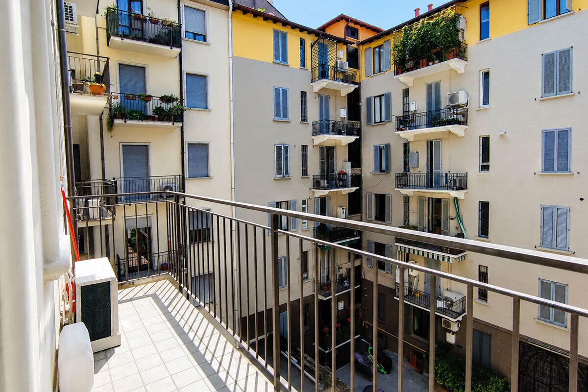 Un edificio residenziale a più piani con balconi, condizionatori d'aria e piante in vaso.