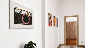 Un corridoio con una pianta in vaso, un quadro con una macchina fotografica e una porta in legno alla fine.