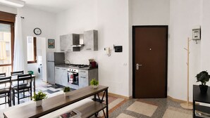 A compact kitchen with modern appliances, a dining area with a bench, and a door leading to another room. - BIG Flat Goldoni [Duomo–M4–Linate] (Milan)