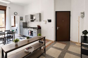 Una cucina compatta con elettrodomestici moderni, una zona pranzo con una panca e un'apertura che dà su un'altra stanza.
