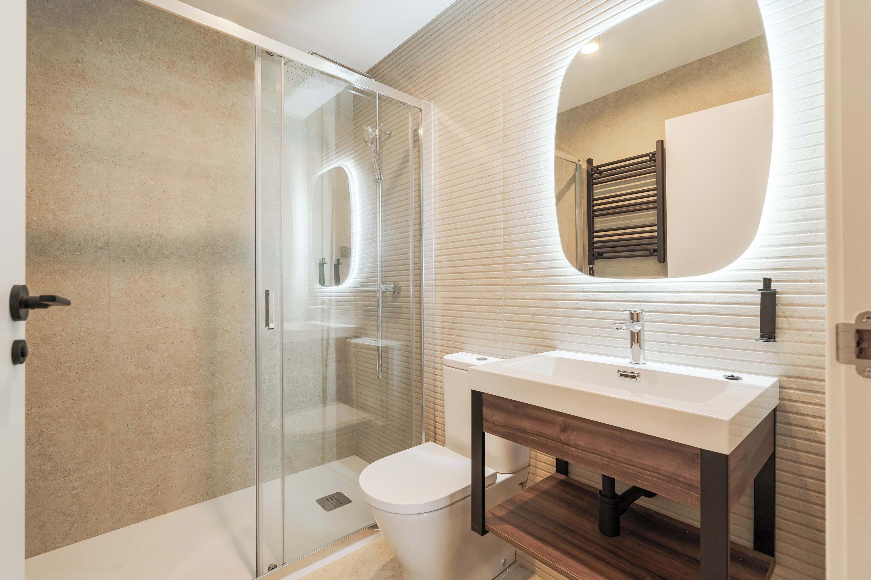 Ein modernes Badezimmer mit einer gläsernen Duschkabine, einem weißen Waschbecken und einem Holzlagerfläche.