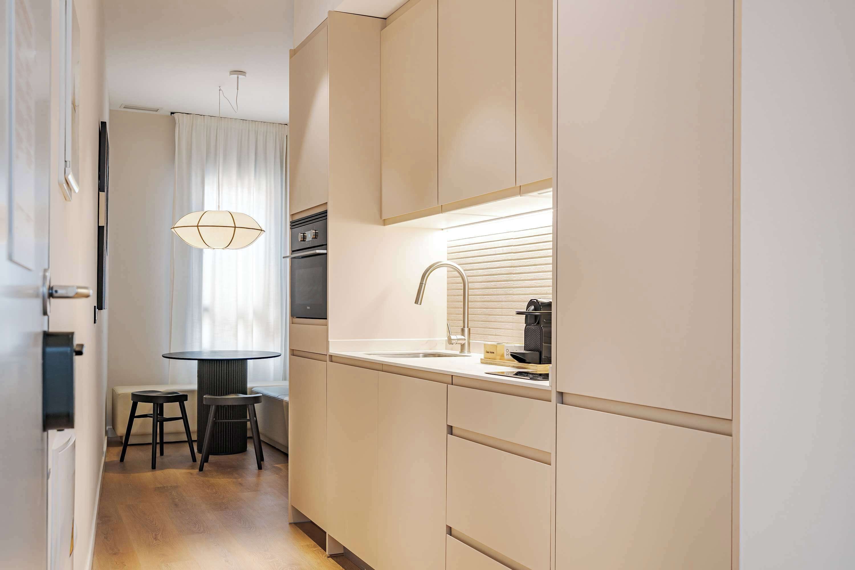 A modern kitchen with light-colored cabinets, a round dining table with stools, and a pendant light.