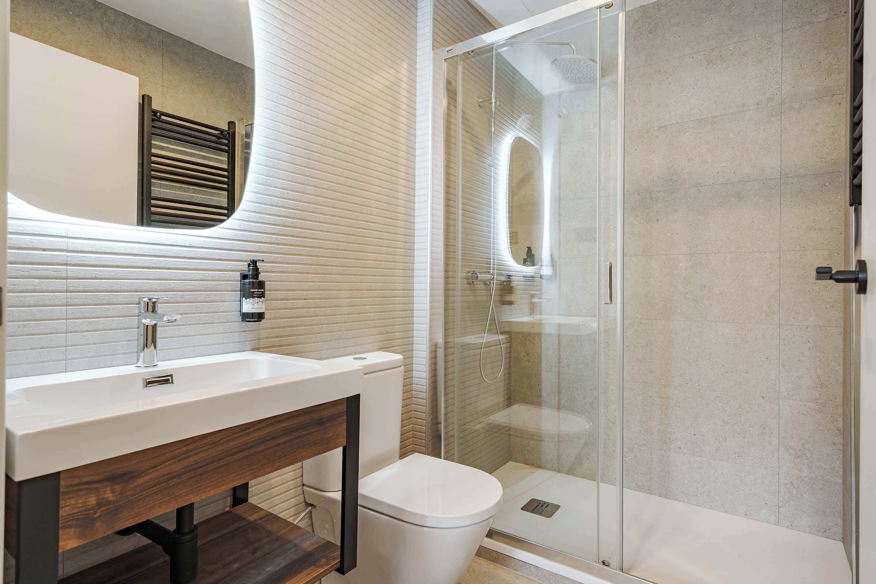 Une salle de bain moderne avec un lavabo blanc, un meuble-lavabo en bois et une cabine de douche en verre.