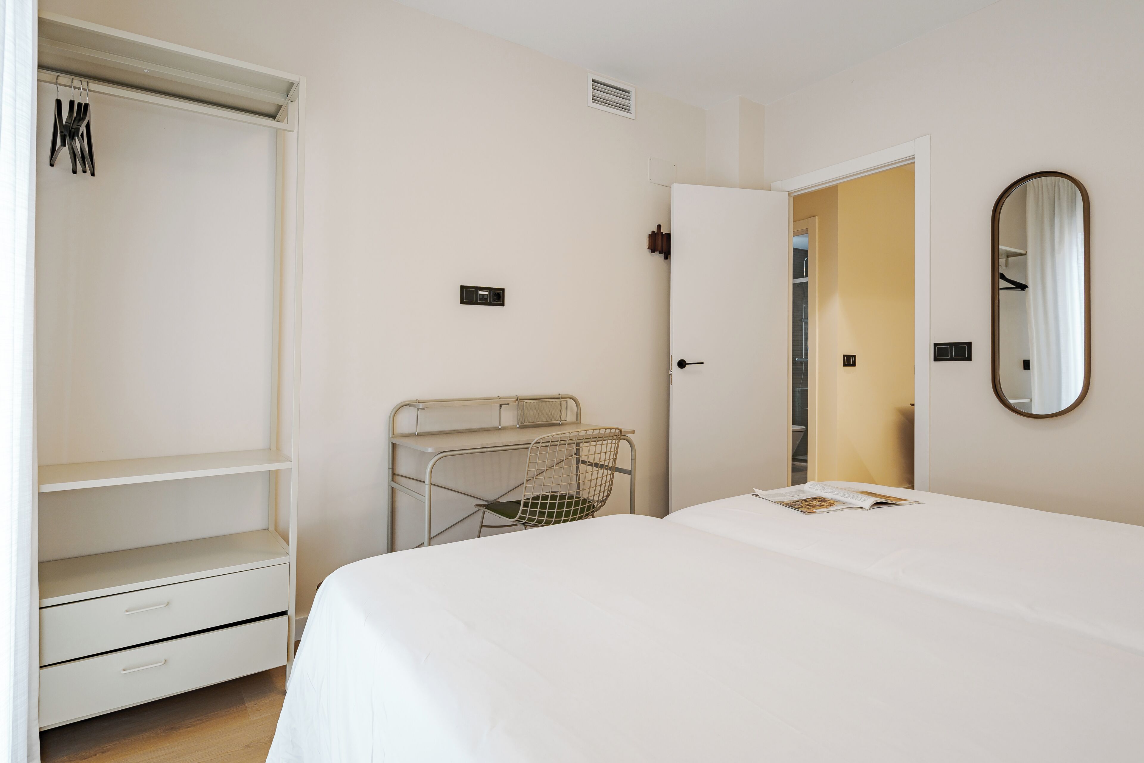 A bedroom with a bed, a wardrobe, a mirror, and a door leading to another room.