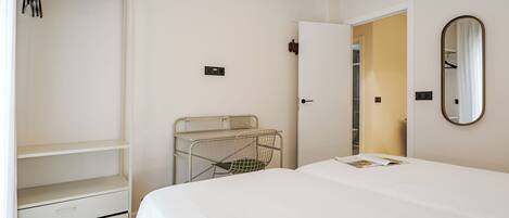 A bedroom with a bed, a wardrobe, a mirror, and a door leading to another room.