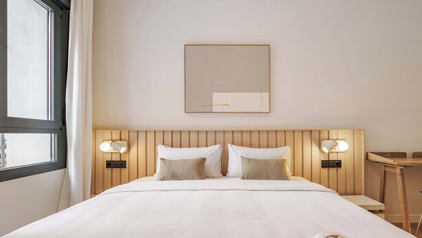 A hotel room with a bed, two bedside lamps, a bedside table, a mirror, and a window. - Numancia Apartments by Olala Homes (Madrid)
