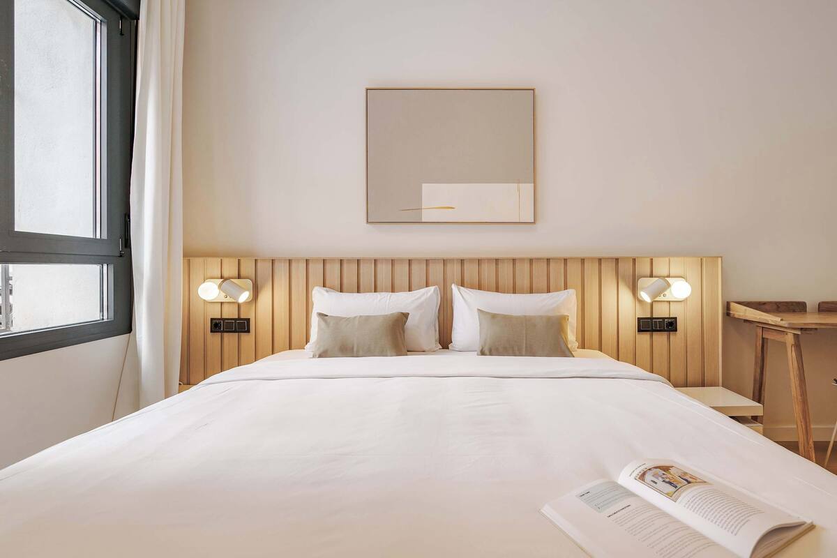 Een hotelkamer met een bed, twee bedlampen, een nachtkastje, een spiegel en een raam.