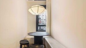 A corner room with a round table, two stools, a bench, a hanging light fixture, and a window with a view. - Numancia Apartments by Olala Homes (Madrid)