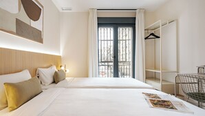 A hotel room with two beds, a wardrobe, a chair, and a window with a view of buildings. - Numancia Apartments by Olala Homes (Madrid)