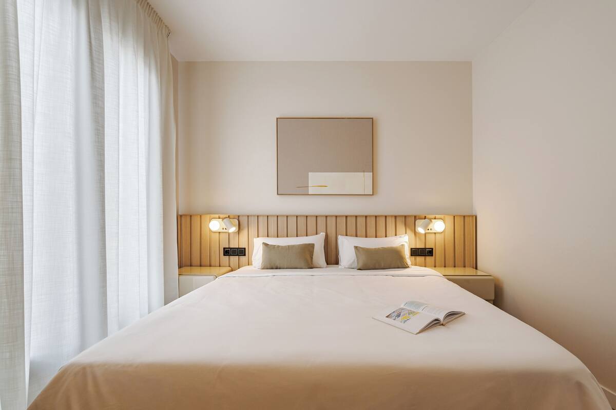 Hotelkamer met een groot bed, twee nachtkastjes met lampen, een spiegel aan de muur en een raam met gordijnen.