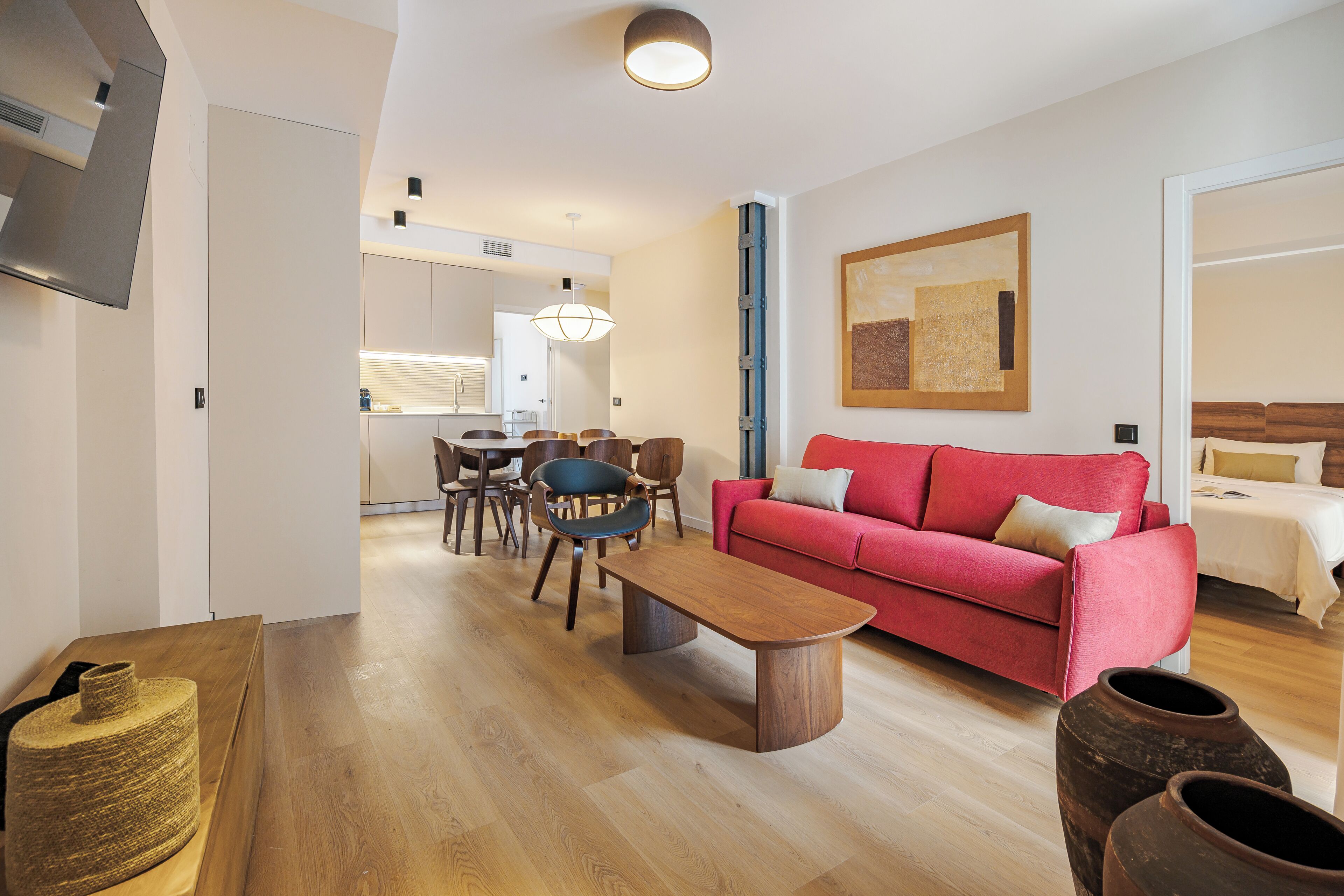 Ein modernes Wohnzimmer mit einem roten Sofa, einem Holztisch und einer Essecke mit Stühlen und Tisch.