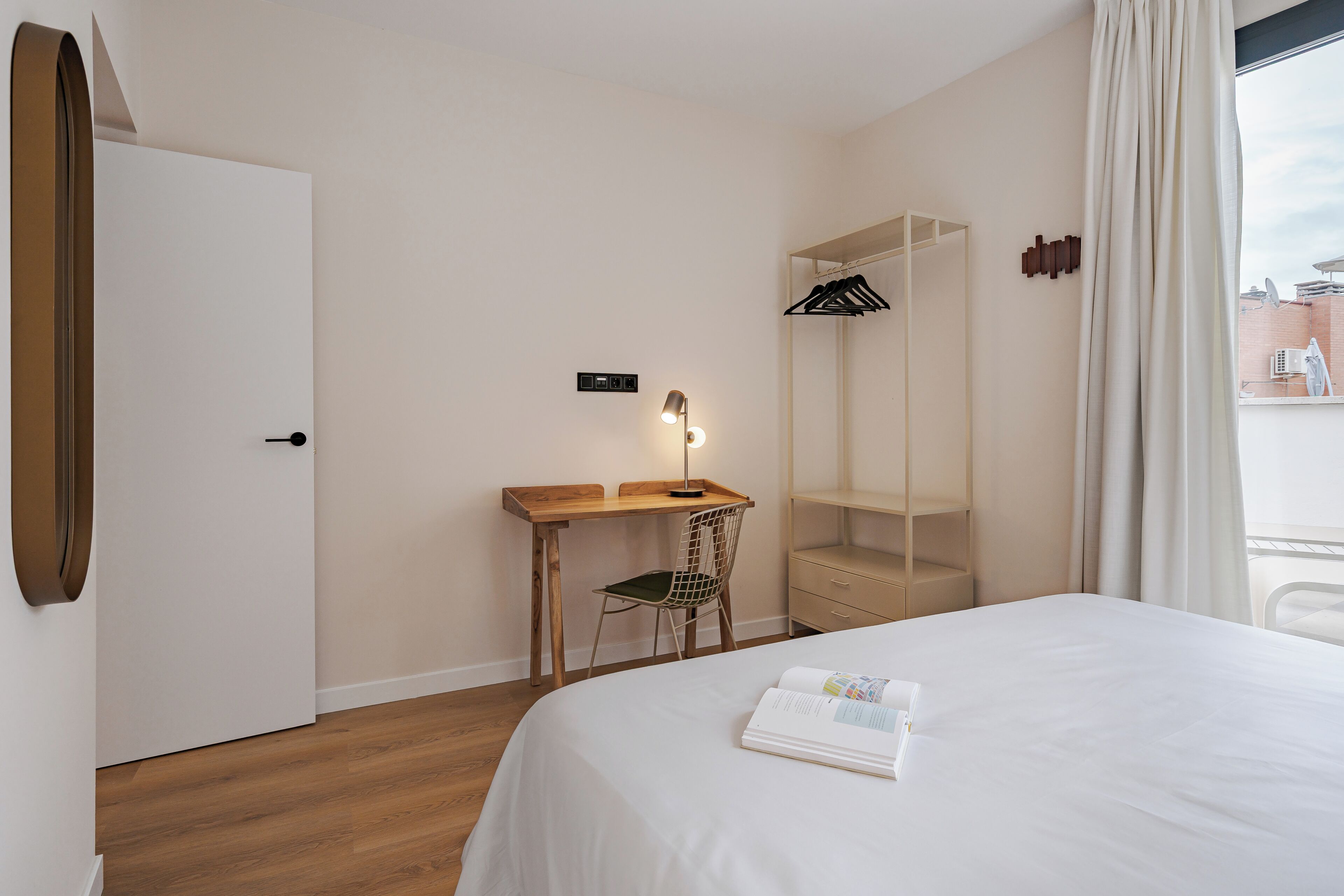 A hotel room with a bed, a desk, a chair, a wardrobe, and a window with curtains.