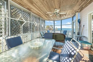 Une terrasse extérieure avec une table et des chaises en verre, un ventilateur de plafond et une vue sur l’océan.