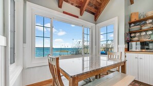 A dining area with a table and chairs, large windows with a view of the sea, and a shelf with dishes. - Lavinder House by Seaside Vacations & Sales! (Chincoteague Island)