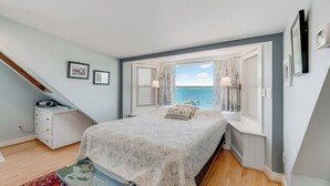 A bedroom with a bed, a dresser, a window with curtains, and a view of the sea. - Lavinder House by Seaside Vacations & Sales! (Chincoteague Island)
