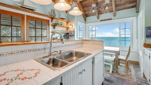 A kitchen with a large island, wooden ceiling beams, and a view of the sea through large windows. - Lavinder House by Seaside Vacations & Sales! (Chincoteague Island)