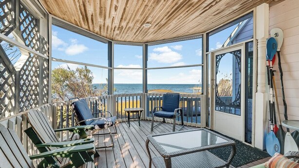 A covered outdoor deck with seating, a glass table, and a view of the ocean. - Lavinder House by Seaside Vacations & Sales! (Chincoteague Island)