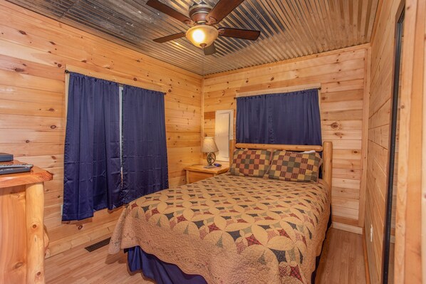 A wooden cabin bedroom with a bed, curtains, a ceiling fan, and a nightstand. - You’ve Earned A Relaxing Gatlinburg Vacation (GATLINBURG)