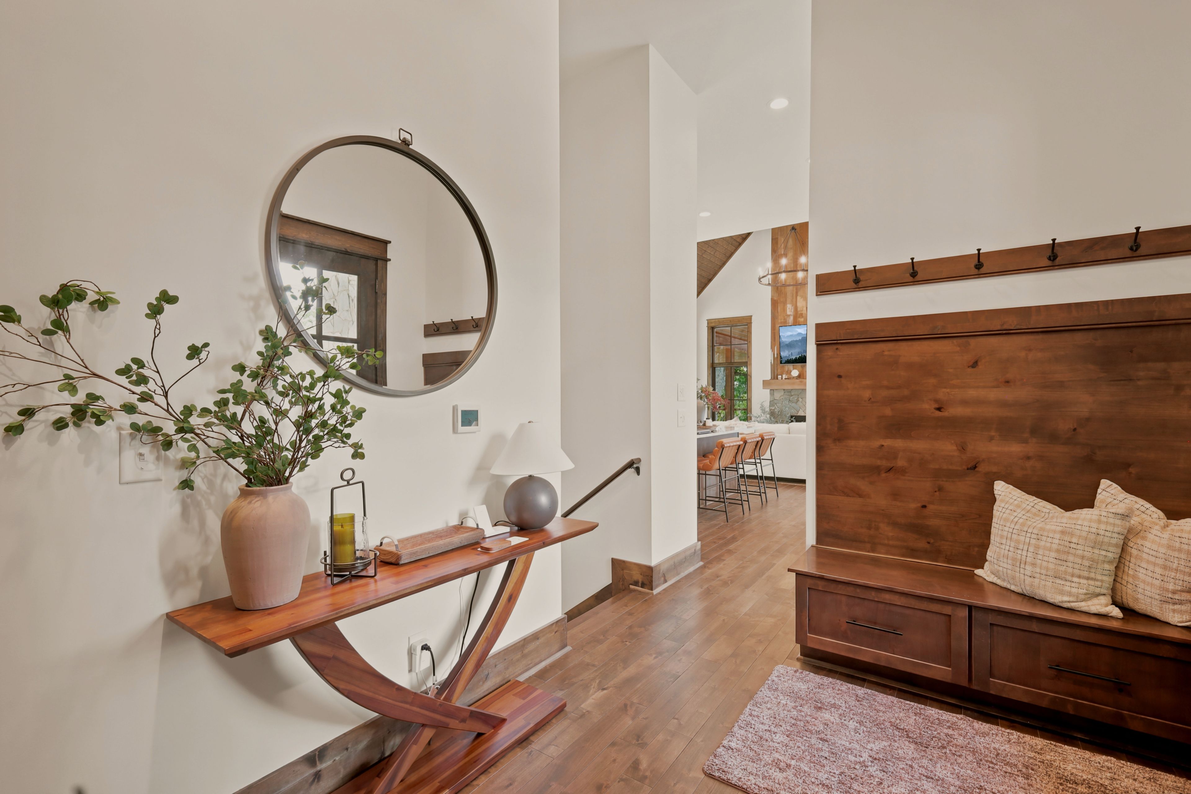 A modern interior with a wooden console table, a round mirror, a potted plant, and a wooden headboard with pillows.