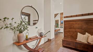 A modern interior with a wooden console table, a round mirror, a potted plant, and a wooden headboard with pillows.