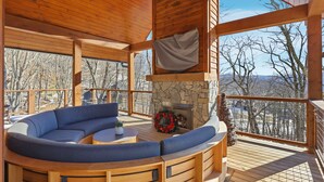 Una terraza de madera con una chimenea de piedra, una zona de estar en forma de curva y vistas del paisaje circundante.