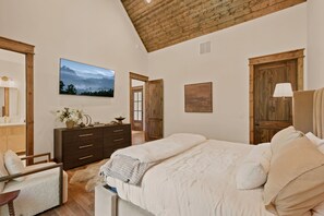 A bedroom with a large bed, wooden wardrobe, a dresser, a mirror, and a painting on the wall. - Brand-New LUXE Creekside Cabin w Hot Tub, Fire Pit (Banner Elk)