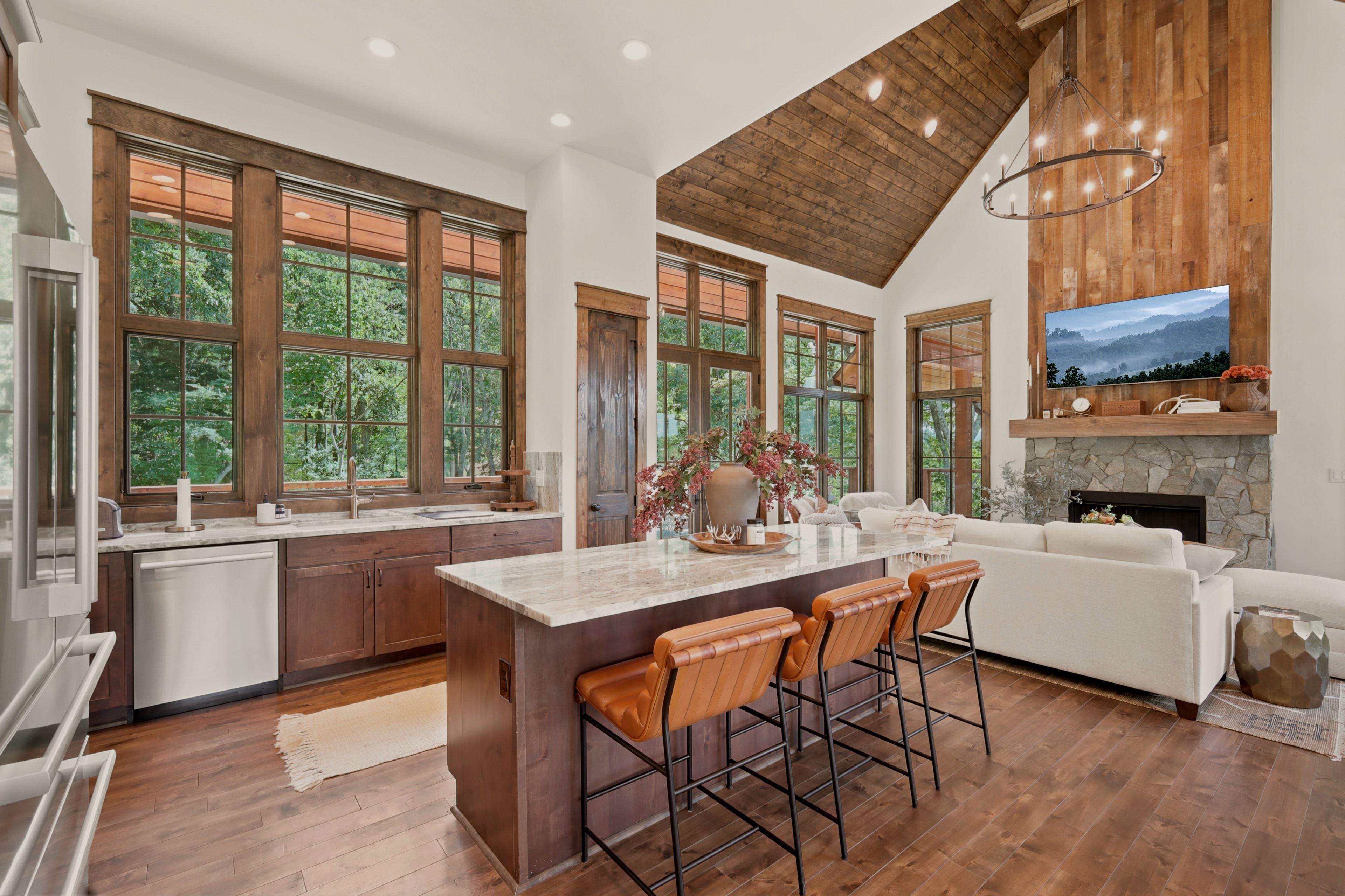 A spacious kitchen with a large island, wooden ceiling, and a stone fireplace.