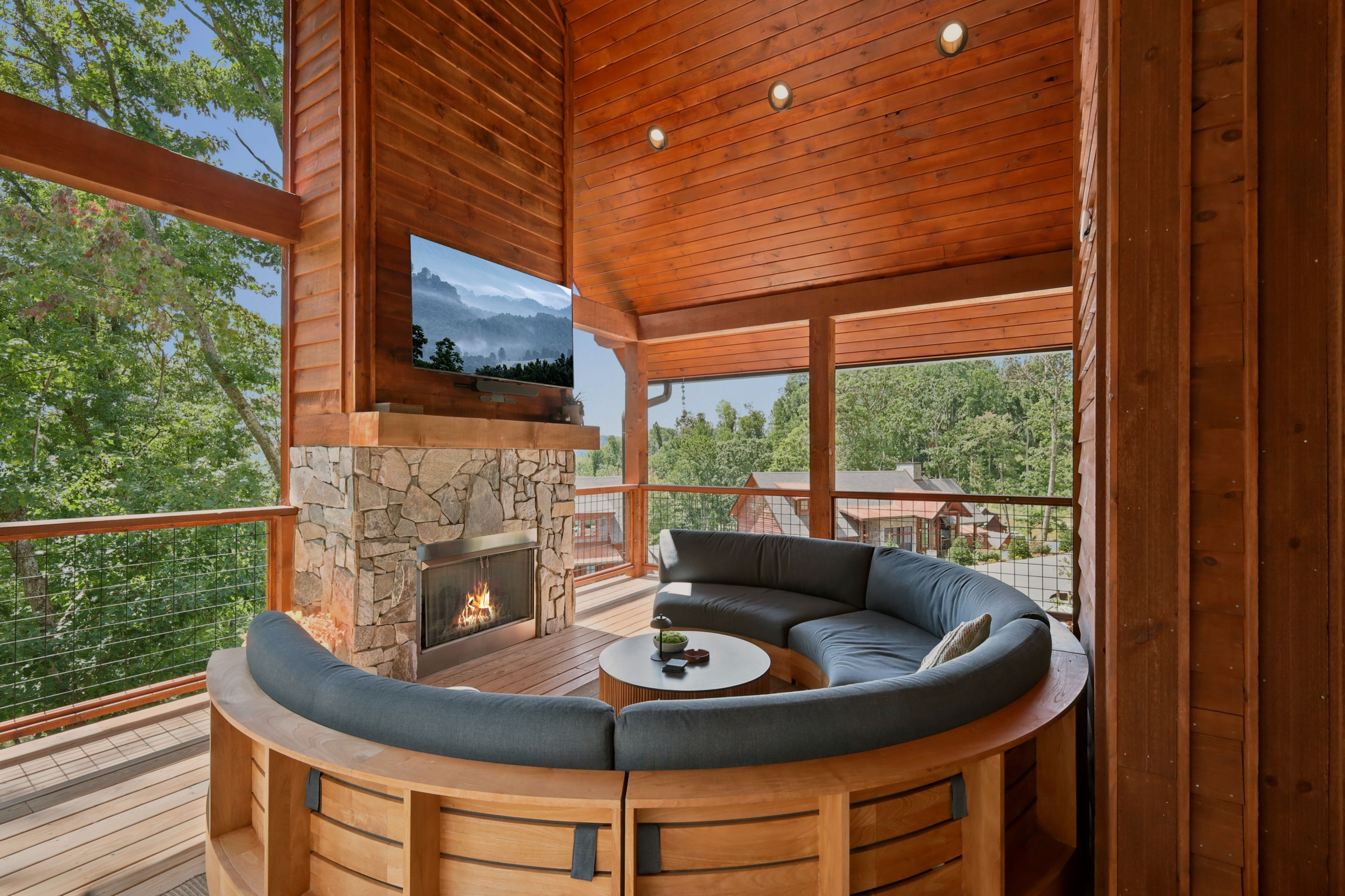 A wooden deck with a stone fireplace, a curved sofa, and a television mounted on the wall.
