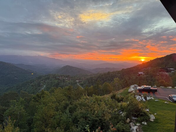 Paisagem montanhosa com um pôr do sol, uma estrada e um edifício com telhado vermelho.