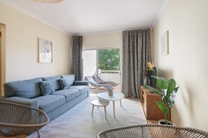 Een woonkamer met een bank, twee stoelen, een bijzettafeltje en een plant in een pot.