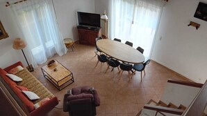 Una sala de estar con sofá, una mesa de centro, televisor, mesa de comedor y sillas, y una escalera.