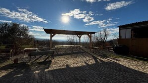 Un espace extérieur abrité, doté d’un sol en pierre, de bancs et d’une pergola, le tout sous un ciel dégagé.