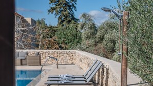 A poolside area with lounge chairs, a stone wall, and a wooden pergola. - Vamos Villa (Apokoronas)