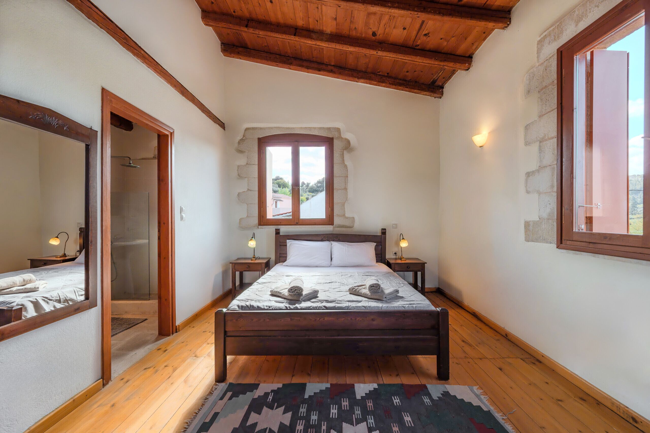 Une chambre avec un plafond en bois, un grand lit avec deux oreillers, une fenêtre et un miroir.