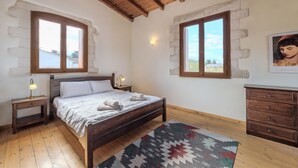 A bedroom with a wooden bed, two bedside tables with lamps, a wooden dresser, and a patterned rug. - Vamos Villa (Apokoronas)